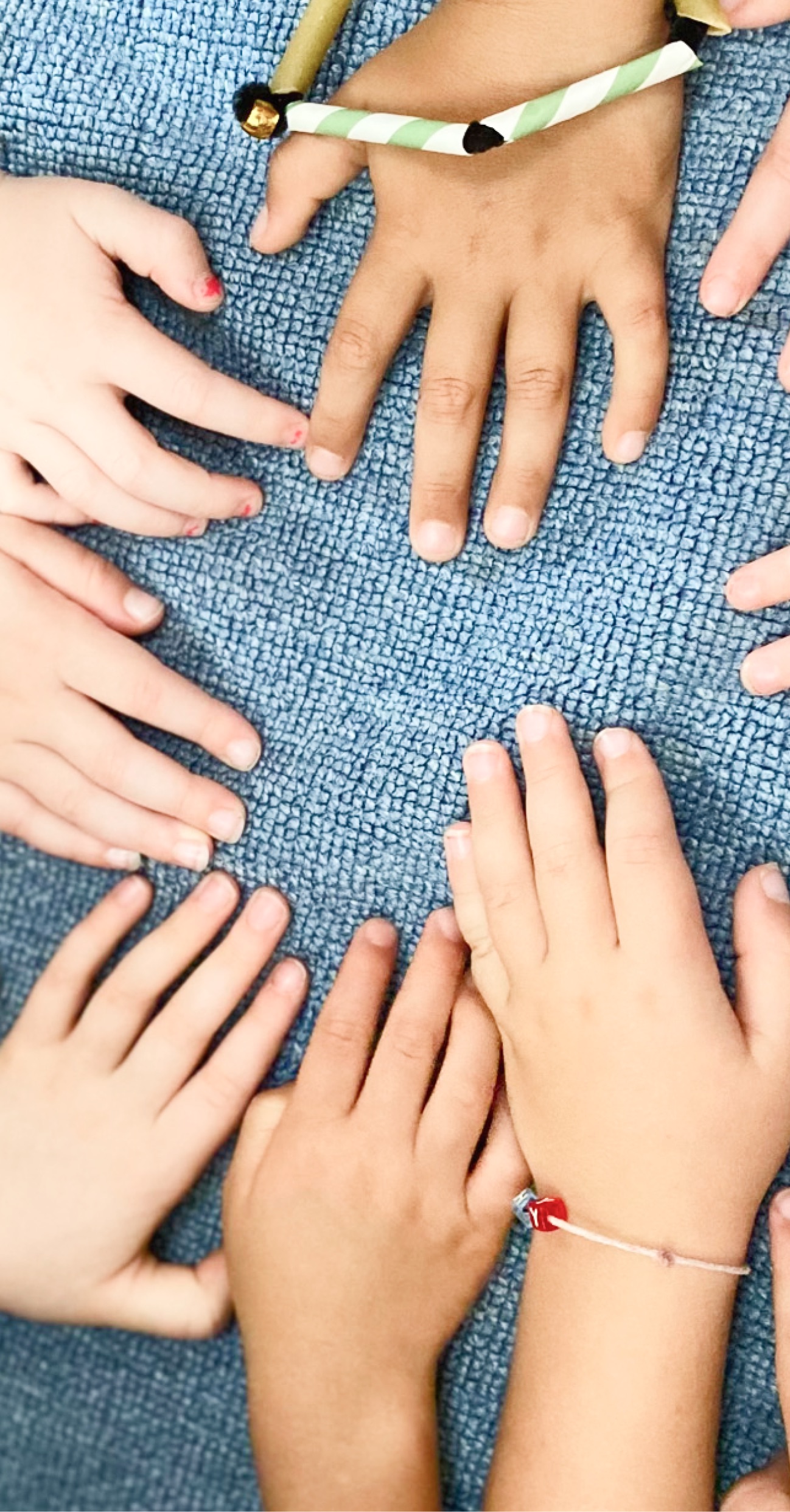 Several children's hands resting together on a blue woven rug