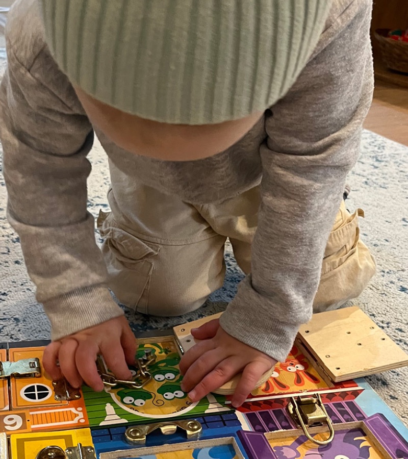 A child kneeling at a floor mat, working with a wooden puzzle map