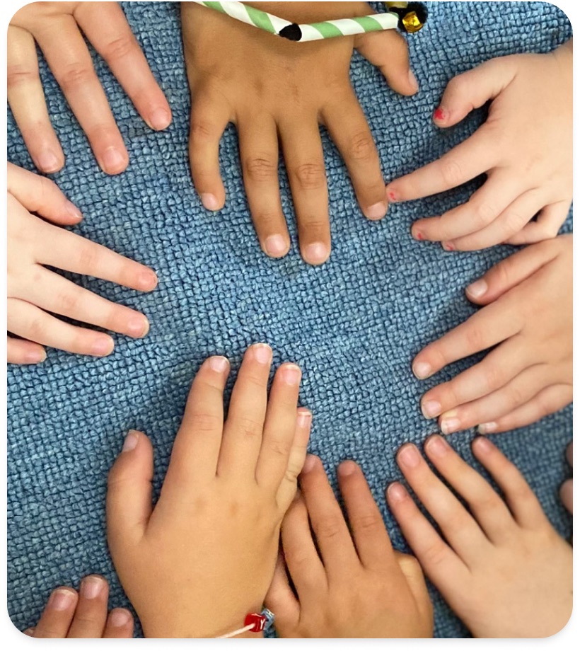 Several children's hands resting together on a blue woven rug