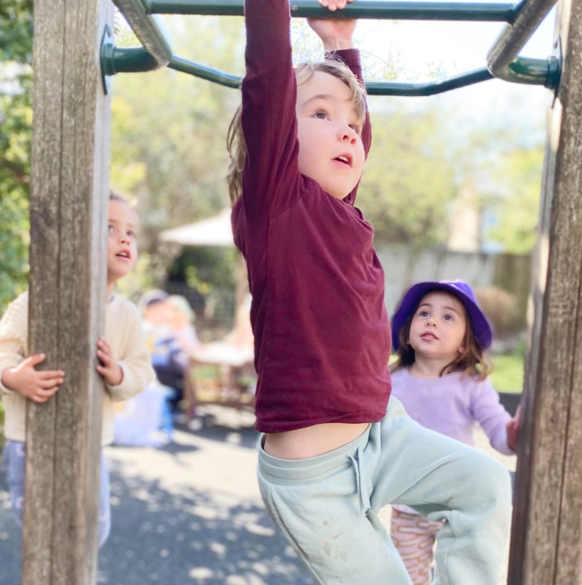A child hanging from the monkey bars in the preschool playground